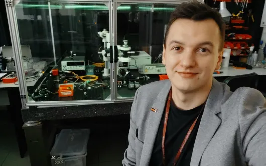 Zdjęcie naukowca na tle światłowodowej aparatury badawczej.