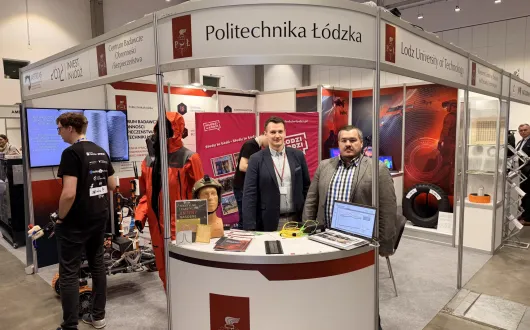 Pracownicy katedry na stanowisku uczelni podczas targów AZYL EXPO 2026, przedstawiający rozwiązania czujników światłowodowych.